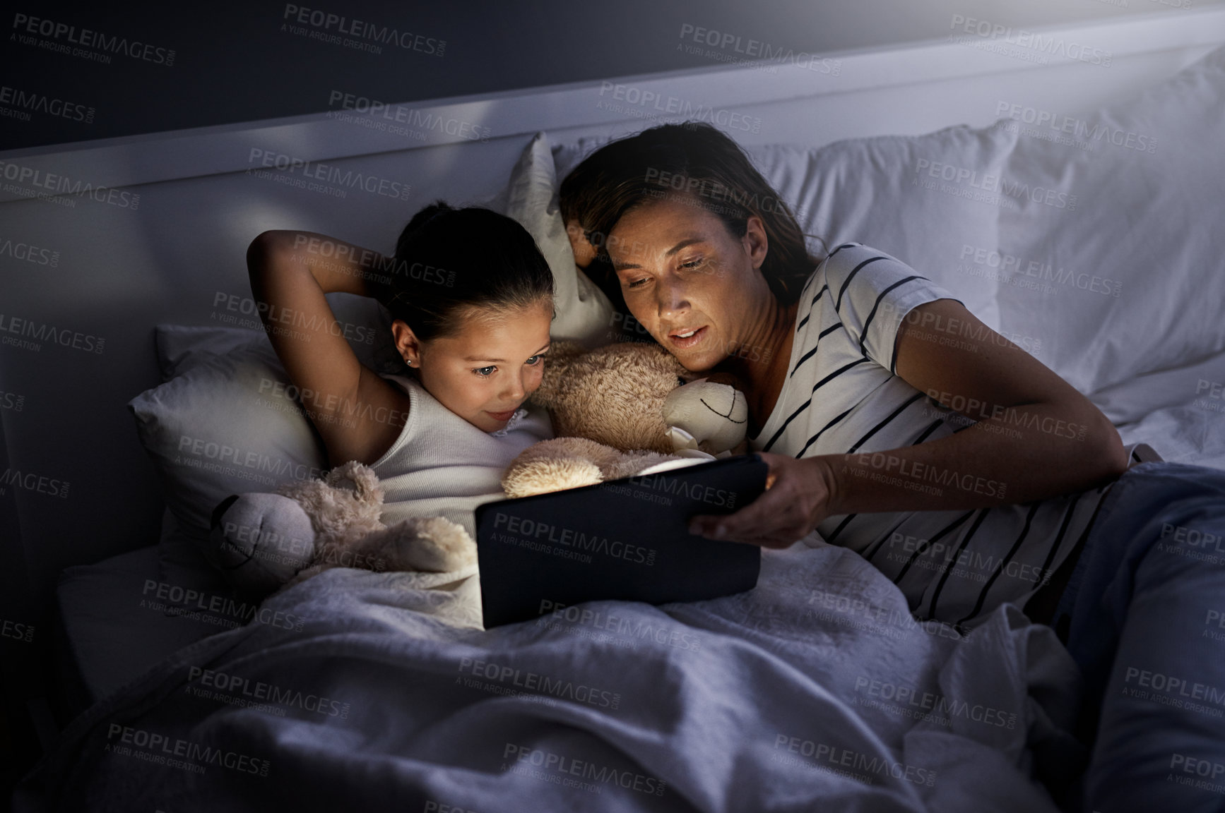 Buy stock photo Shot of a mother and her little daughter using a digital tablet together in bed at night