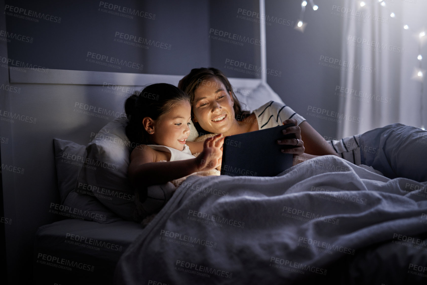 Buy stock photo Shot of a mother and her little daughter using a digital tablet together in bed at night