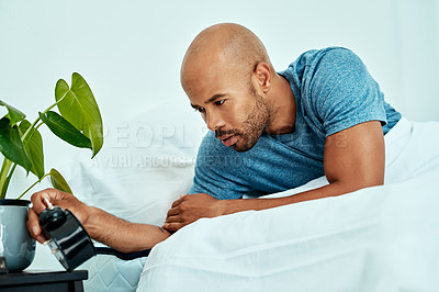 Buy stock photo Cropped shot of a man looking at his alarm clock while lying in bed