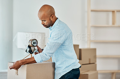 Buy stock photo Shot young man sealing a box while moving house