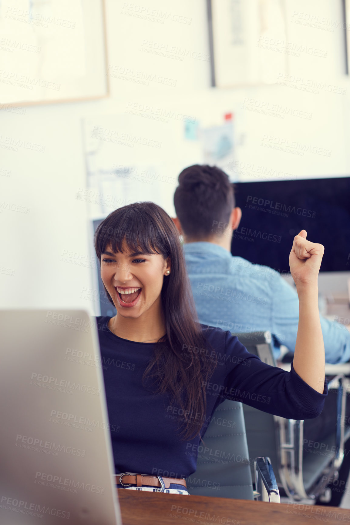 Buy stock photo Shot of a young businesswoman cheering while using a computer at her desk in a modern office