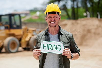 Buy stock photo Cropped portrait of a handsome mature construction worker holding a hiring sign while standing on a construction site