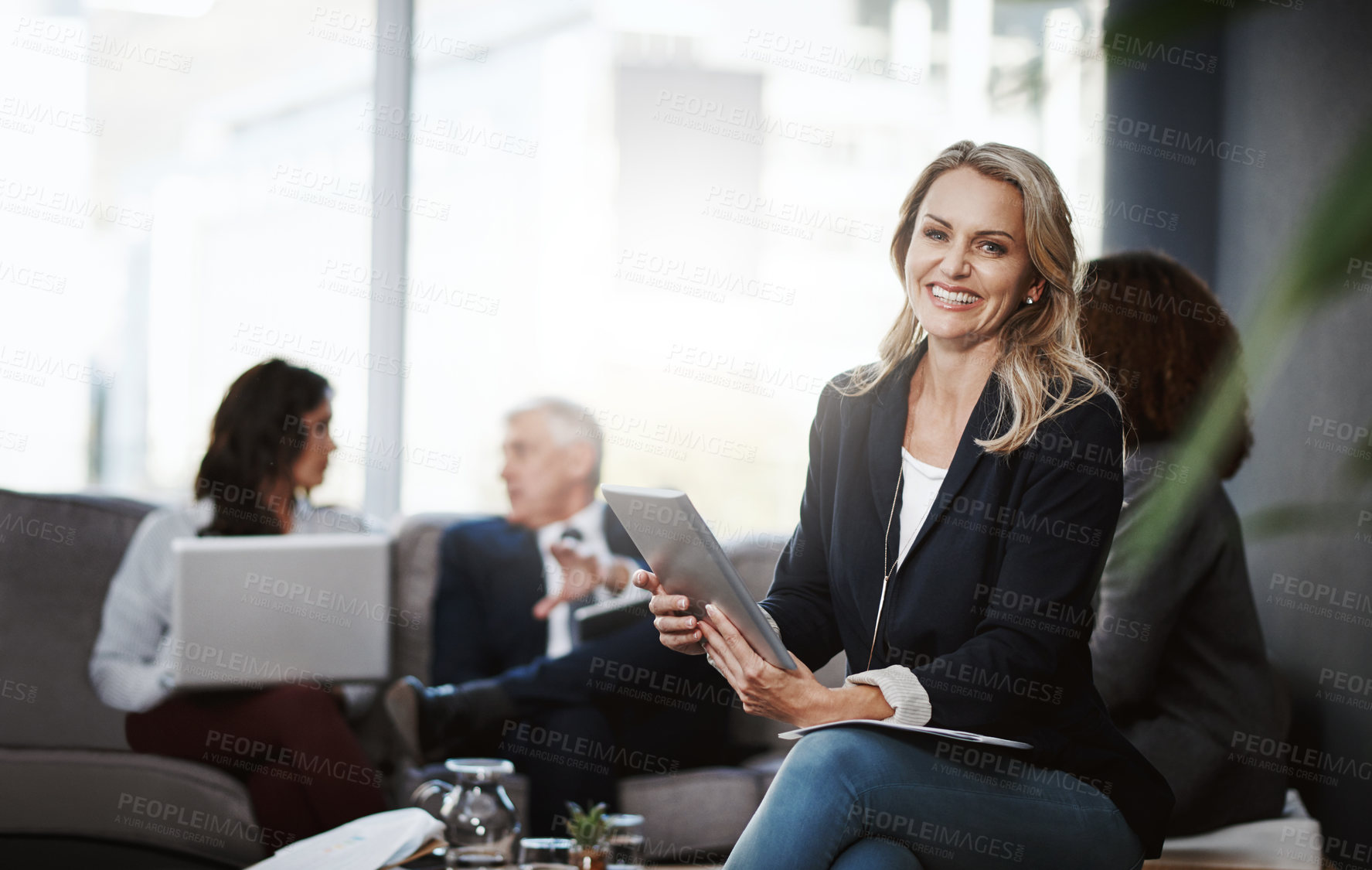 Buy stock photo Portrait of a mature businesswoman using a digital tablet in an office with her colleagues in the background
