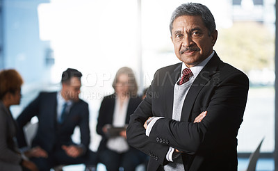Buy stock photo Cropped portrait of a handsome mature businessman standing with his arms folded with his colleagues in the background