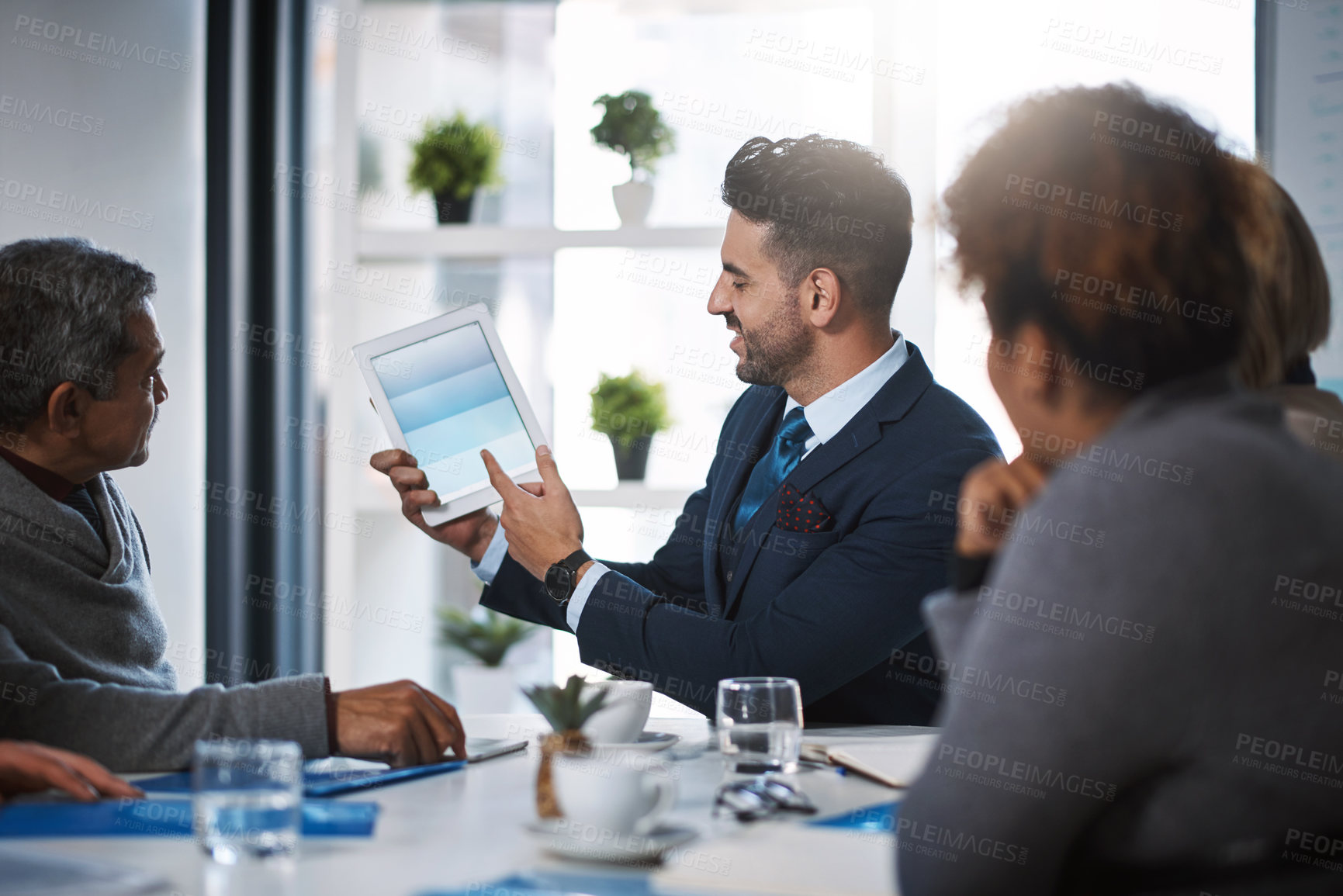 Buy stock photo Cropped shot of a handsome young businessman showing his colleagues something on a tablet during a meeting in the boardroom