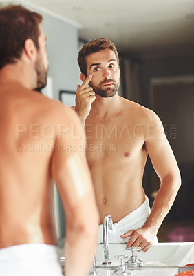 Buy stock photo Cropped shot of a shirtless young man checking out his eye in the bathroom mirror