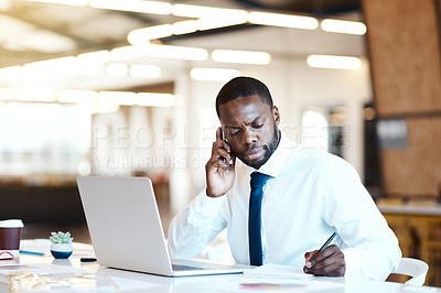 Buy stock photo Shot of a focused young businessman talking on his cellphone and making notes while being seated at his desk in the office during the day