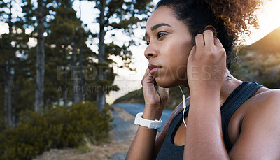 Buy stock photo Shot of a sporty young woman listening to music while exercising outdoors