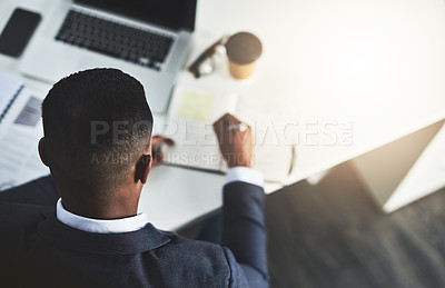 Buy stock photo High angle shot of an unrecognizable young businessman taking notes while working in his modern office