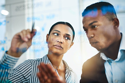 Buy stock photo Shot of two businesspeople brainstorming with notes on a glass wall in an office