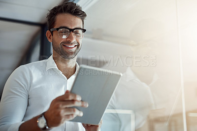 Buy stock photo Cropped shot of a handsome young businessman working on his digital tablet while standing in the office