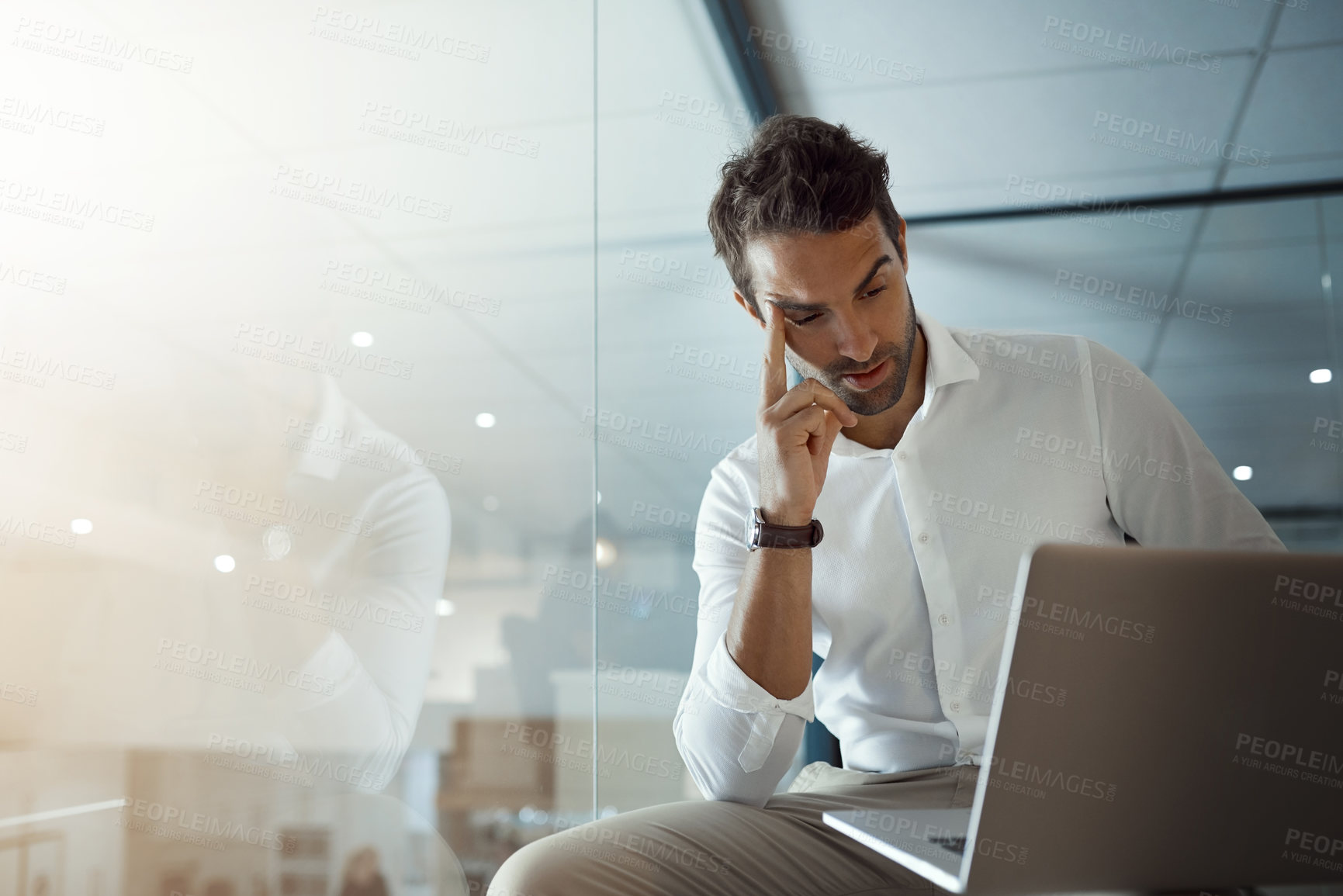 Buy stock photo Cropped shot of a handsome young businessman looking thoughtful while working on his laptop in the office