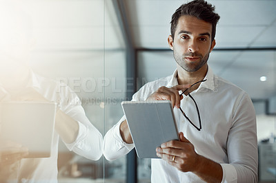 Buy stock photo Cropped portrait of a handsome young businessman working on his digital tablet while standing in the office
