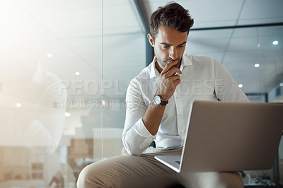 Buy stock photo Cropped shot of a handsome young businessman looking thoughtful while working on his laptop in the office