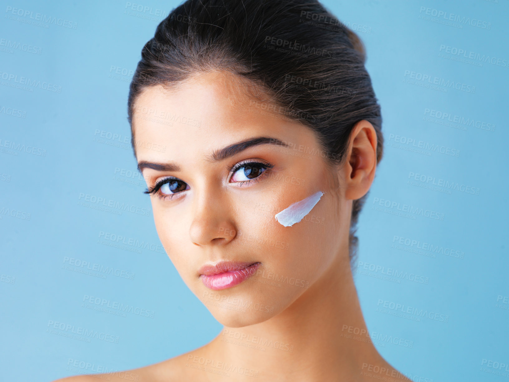Buy stock photo Studio portrait of a beautiful young woman with lotion on her face against a blue background