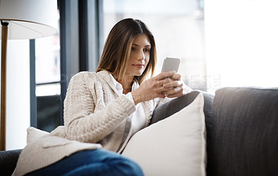 Buy stock photo Shot of a beautiful young woman using her cellphone while relaxing at home