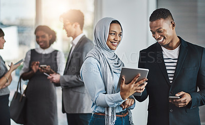 Buy stock photo Shot of a group of young cheerful businesspeople browsing on digital devices while working together in the office at work