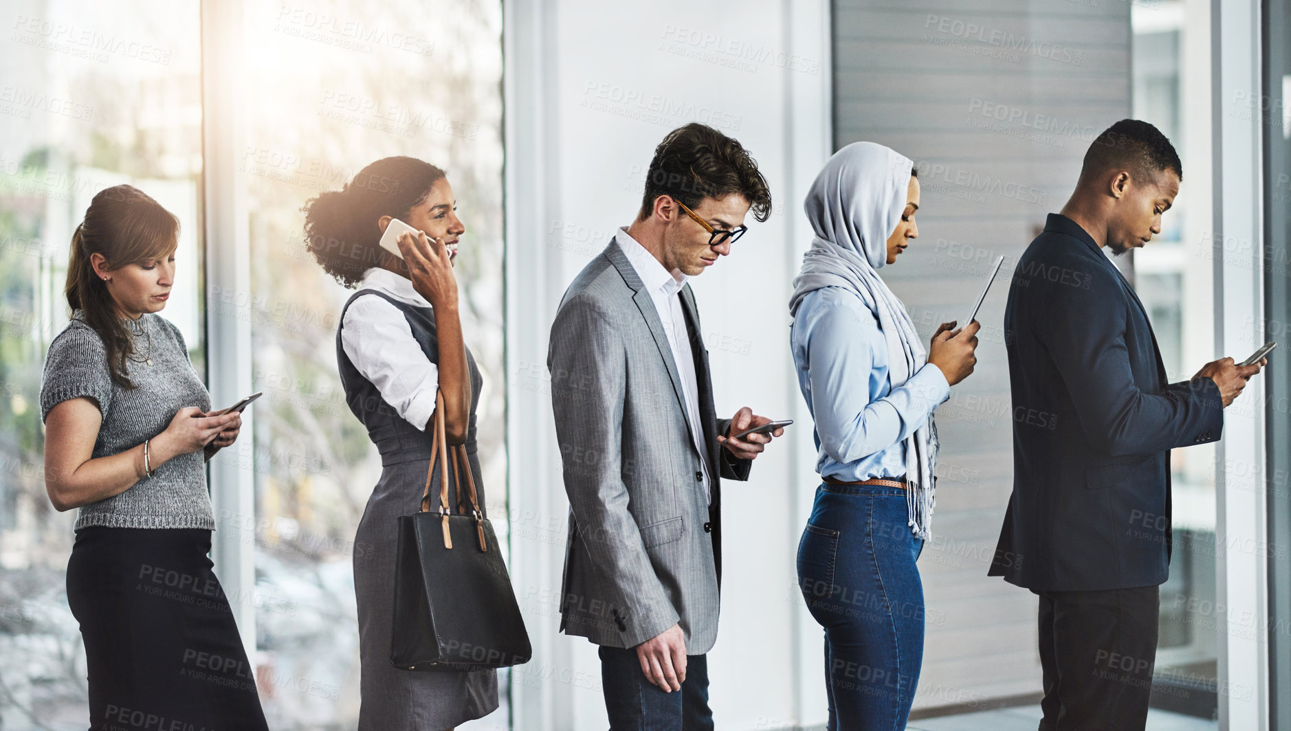 Buy stock photo Shot of a group of businesspeople standing in a row while texting on their phones in the office at work during the day