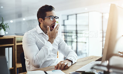 Buy stock photo Shot of a young businessman yawning while working in an office