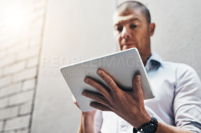 Buy stock photo Low angle shot of a handsome young man using his tablet outside