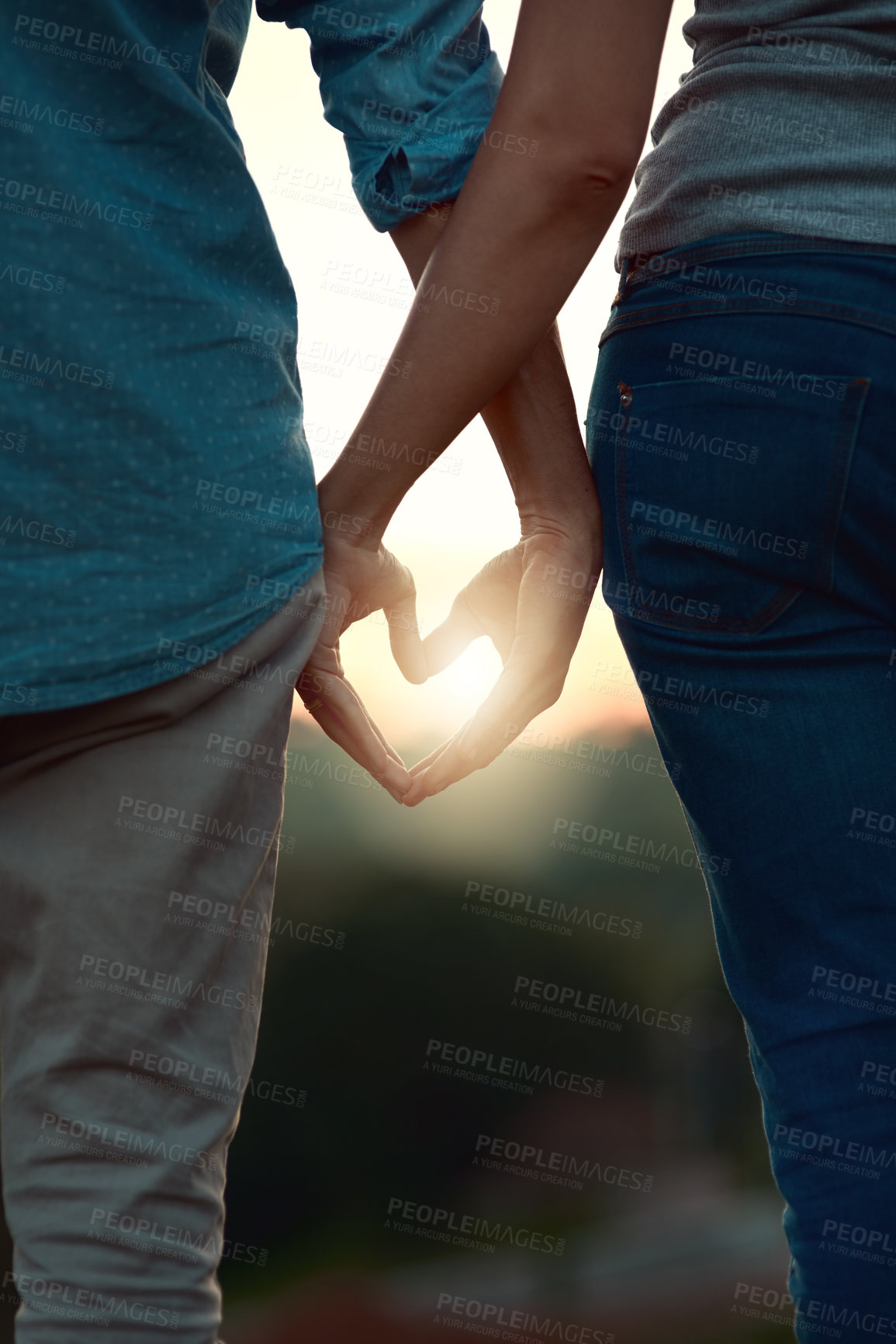 Buy stock photo Rearview shot of an unrecognizable young couple making a heart shape with their hands while standing outside