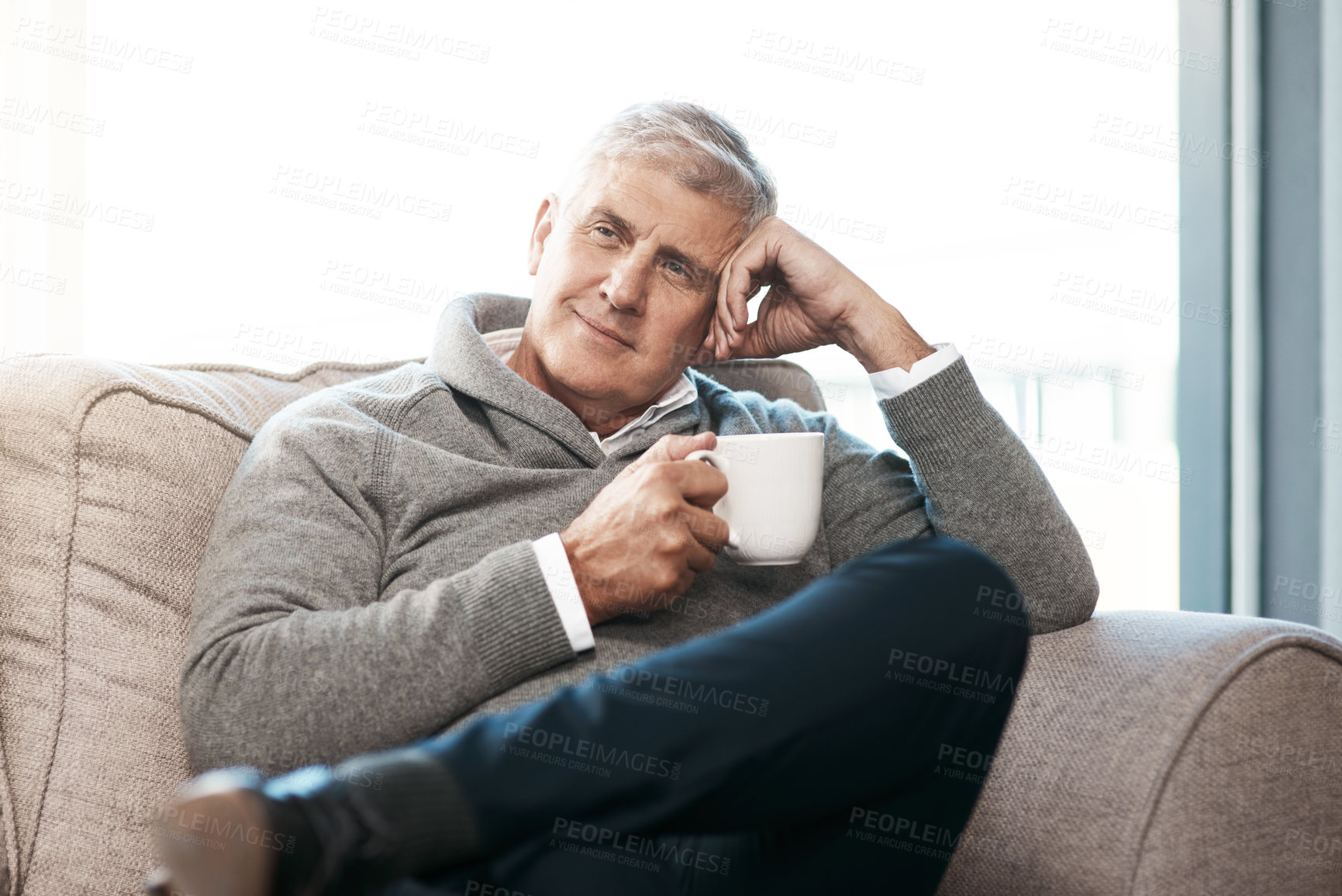 Buy stock photo Cropped shot of a handsome mature man enjoying a coffee while looking thoughtful on the sofa at home