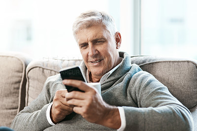 Buy stock photo Cropped shot of a handsome mature man enjoying a coffee while reading a text on the sofa at home