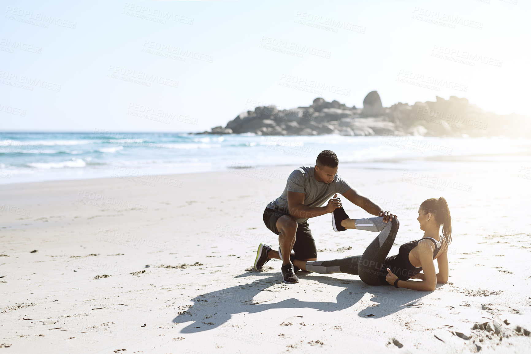 Buy stock photo Shot of a sporty young couple stretching while exercising along the beach