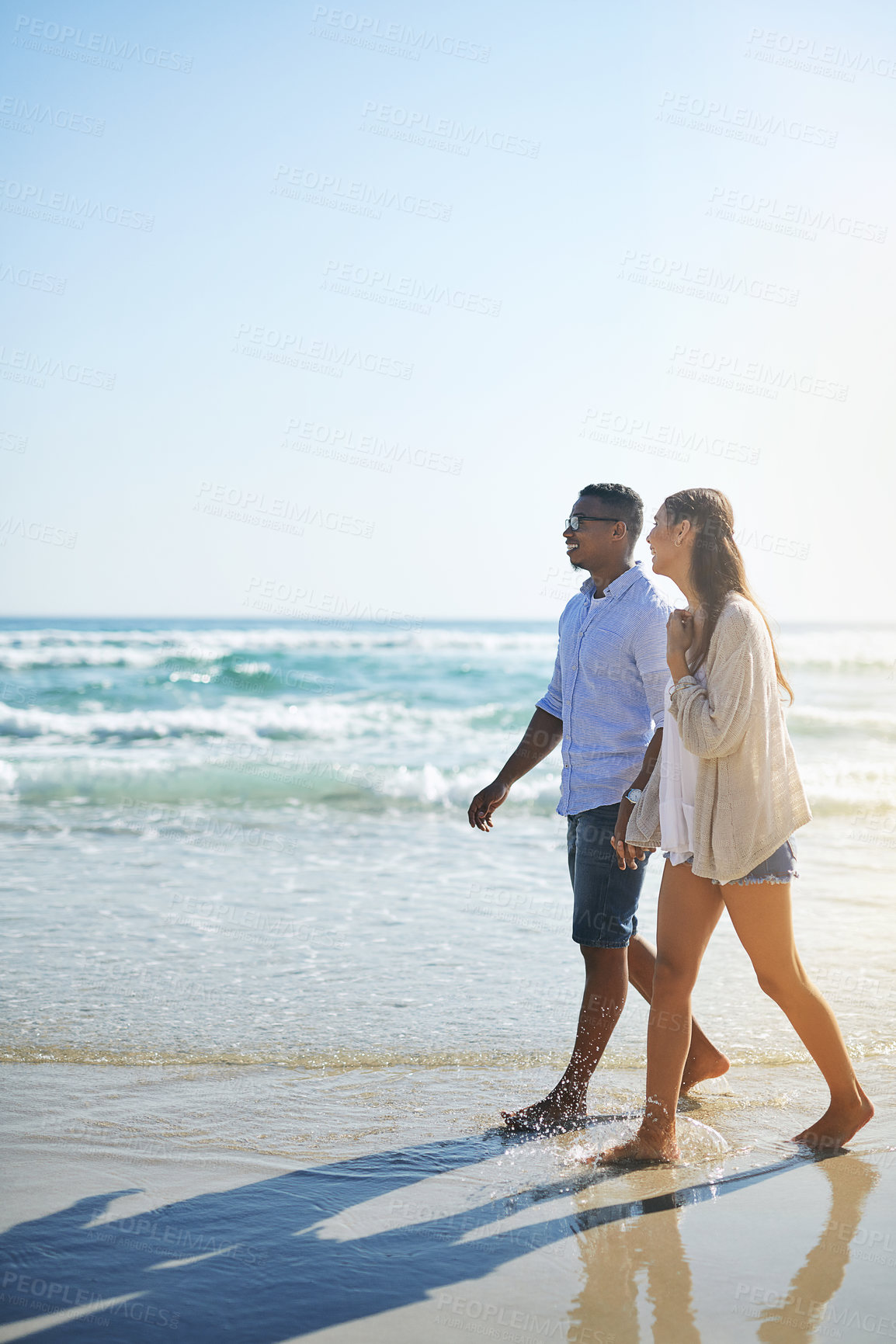 Buy stock photo Shot of a young couple taking a stroll along the beach