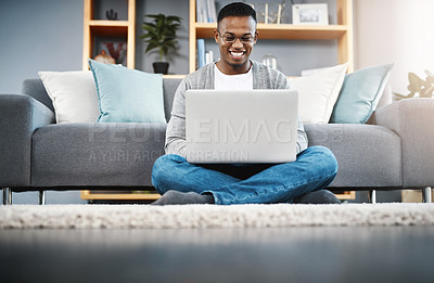 Buy stock photo Shot of a happy young man using a laptop while relaxing at home