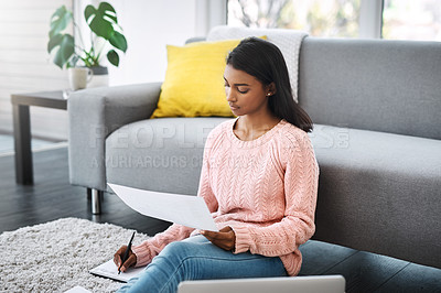 Buy stock photo Cropped shot of a young beautiful woman going through paperwork and using a laptop while sitting on the floor in the living room at home