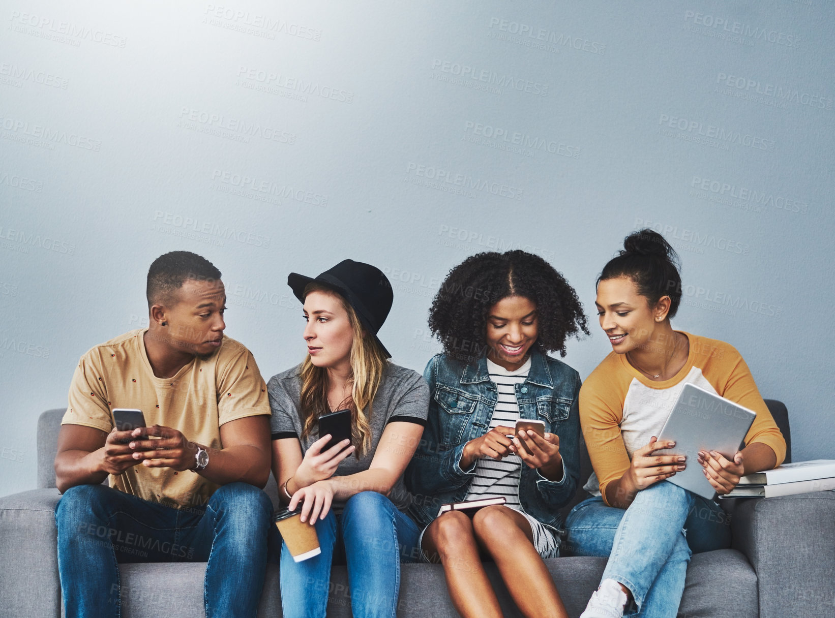 Buy stock photo Studio shot of young people sitting on a sofa and using wireless technology against a gray background