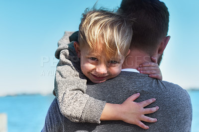 Buy stock photo Portrait of a cheerful little boy being held by his father while they stand next to a beach outside during the day