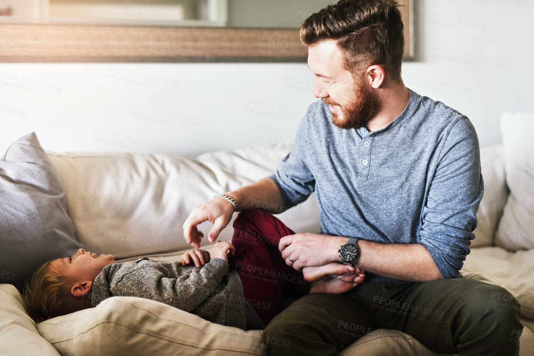 Buy stock photo Shot of a cheerful young man tickling his little boy while they hang out on the sofa at home during the day