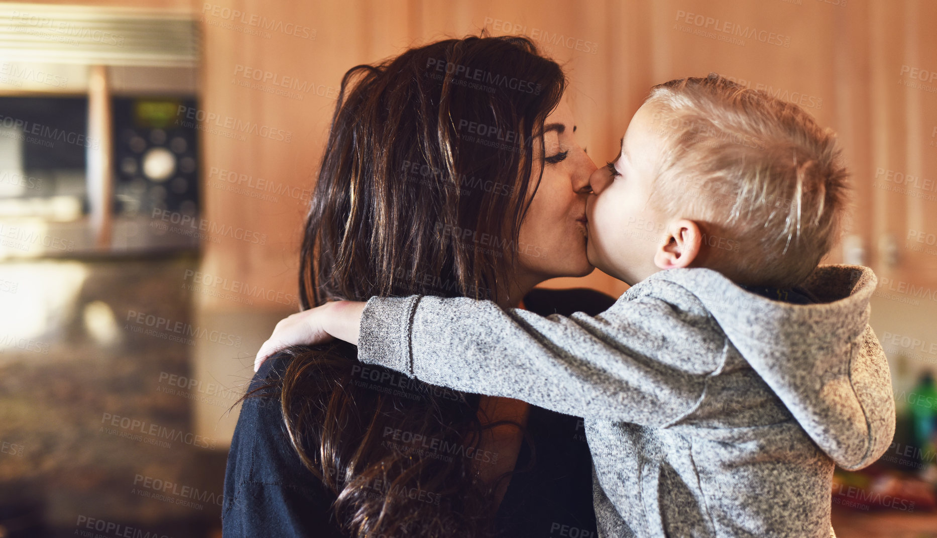 Buy stock photo Shot of a cheerful little boy giving his mother a little kiss at home during the day