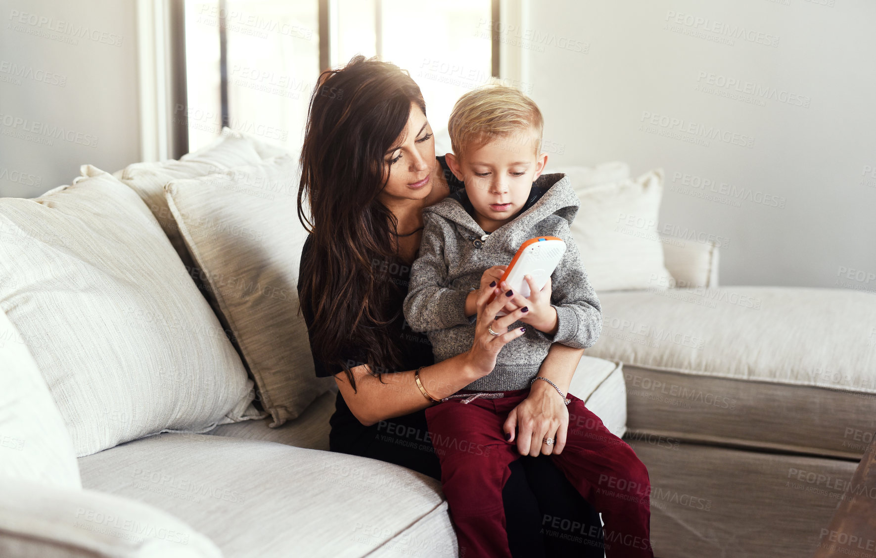 Buy stock photo Shot of a carefree young woman browsing on a cellphone with her little boy while being seated on a sofa at home during the day
