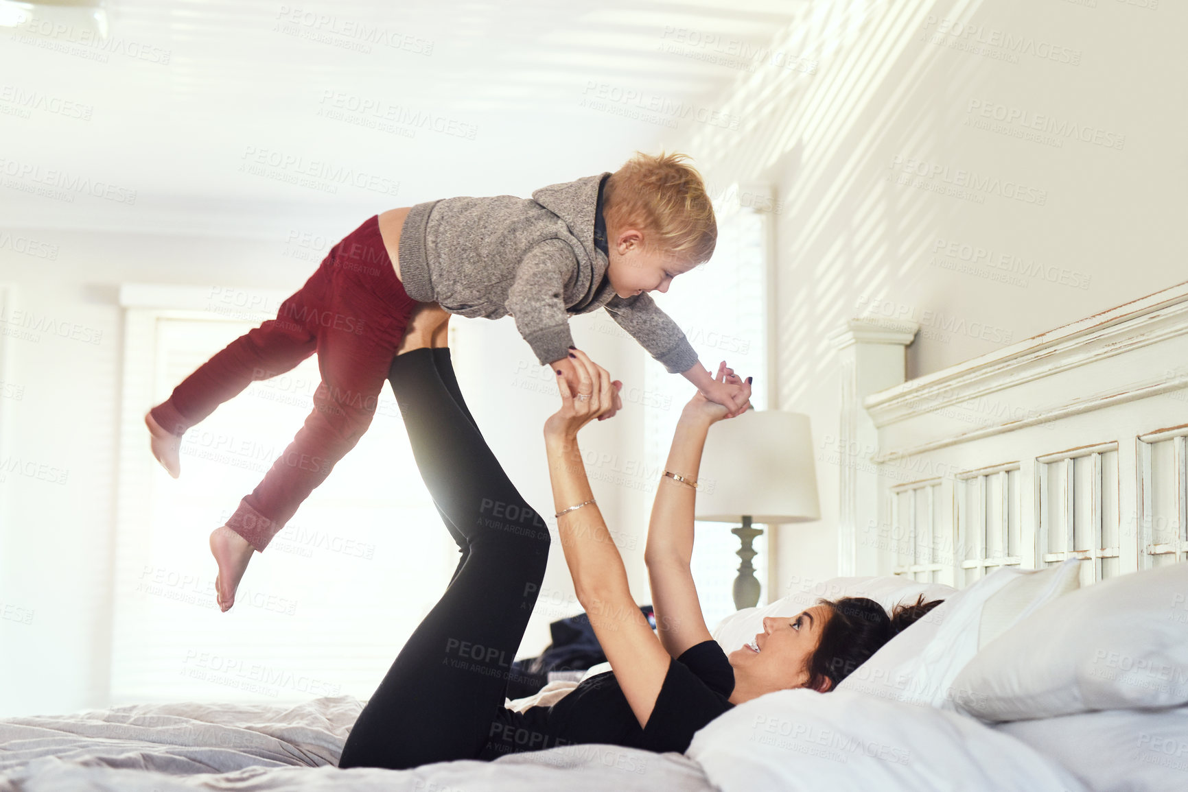 Buy stock photo Shot of a cheerful little boy being lifted up in the air by his mother's legs in the bedroom at home during the day