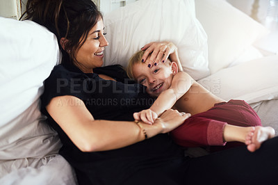 Buy stock photo Shot of a cheerful little boy and his mother hanging out on the bed at home while relaxing during the day