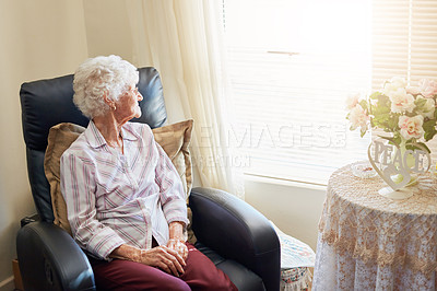 Buy stock photo Shot of an elderly woman relaxing on a chair at home and looking thoughtfully out the window