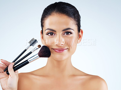 Buy stock photo Studio portrait of an attractive young woman holding makeup brushes against a gray background