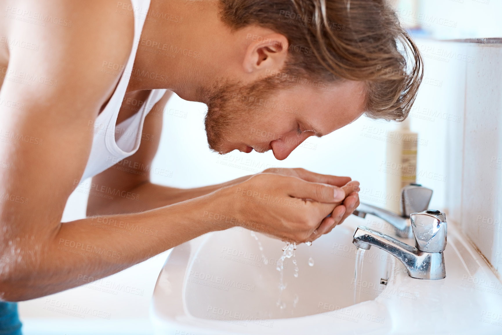 Buy stock photo Shot of a young man washing his face at a basin in the bathroom