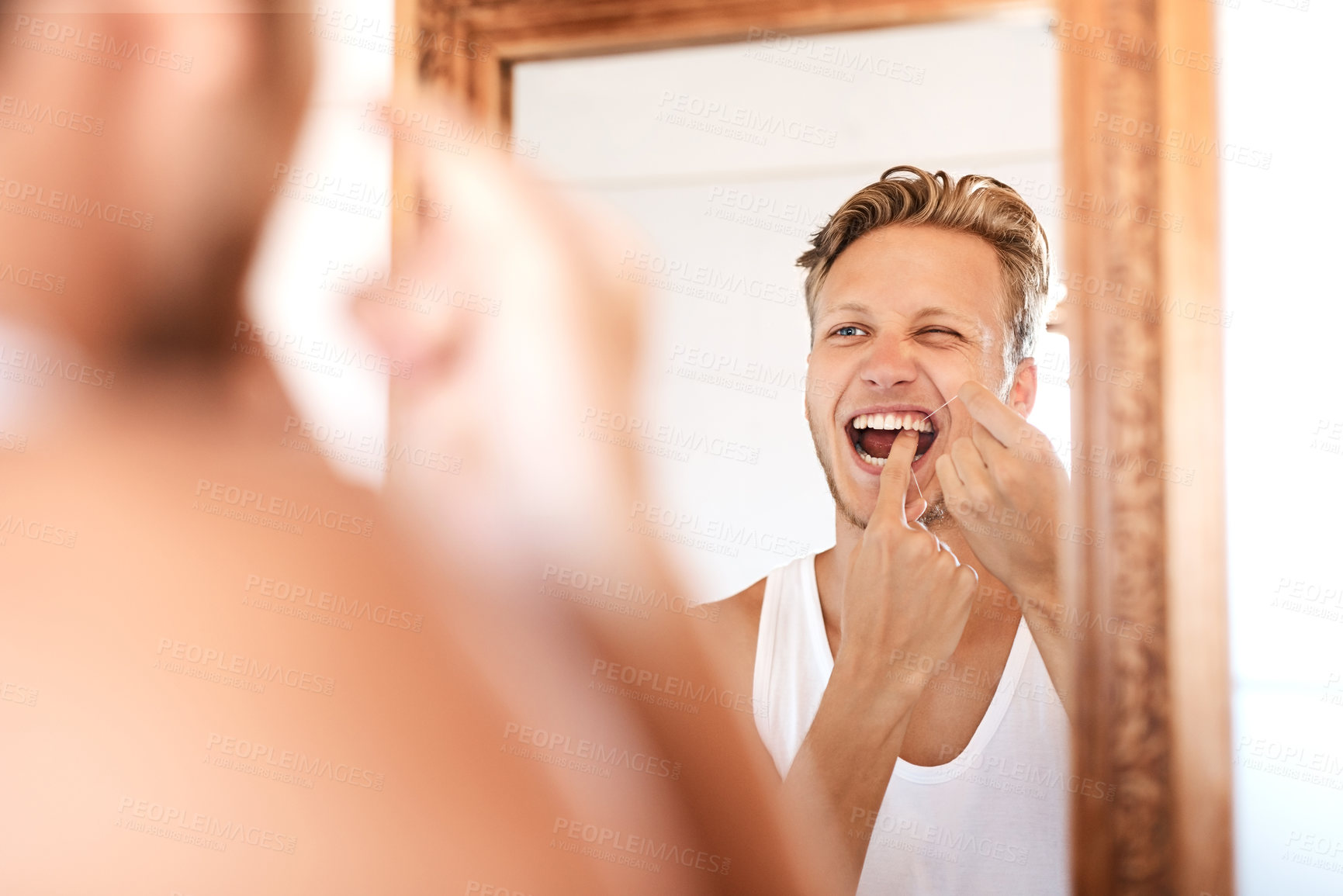 Buy stock photo Shot of a young man flossing his teeth at home