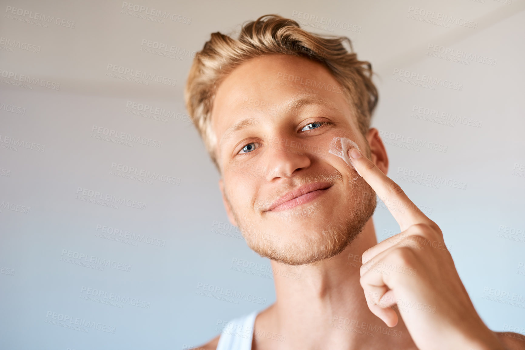 Buy stock photo Portrait of a young man applying moisturizer to his face at home