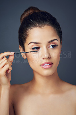 Buy stock photo Studio shot of a beautiful young woman applying mascara while posing against a blue background
