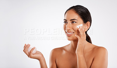Buy stock photo Studio shot of a beautiful young woman applying lotion while posing against a gray background