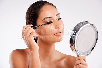 Buy stock photo Studio shot of a beautiful young woman applying mascara using a handheld mirror against a gray background