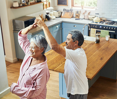 Buy stock photo Shot of a cheerful elderly couple dancing in the kitchen together at home during the day