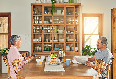Buy stock photo Shot of a cheerful elderly couple having breakfast together around a table at home during the day