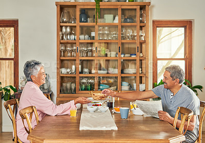 Buy stock photo Shot of a cheerful elderly couple having breakfast together around a table at home during the day