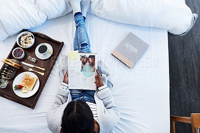 Buy stock photo High angle shot of an unrecognizable woman reading a magazine and having breakfast on her bed in her bedroom at home